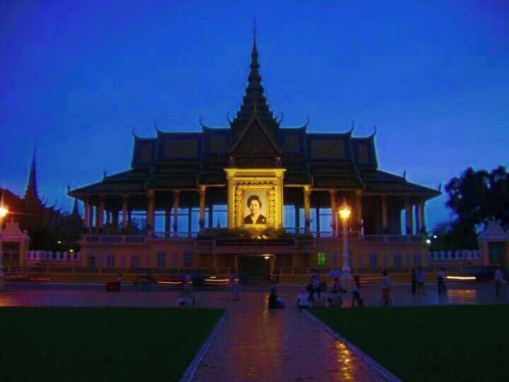 A traditional temple with a central statue, surrounded by a reflective water body and illuminated by evening lights.