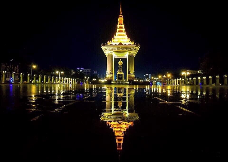 A night-time view of a brightly lit pagoda with a reflection in the water.