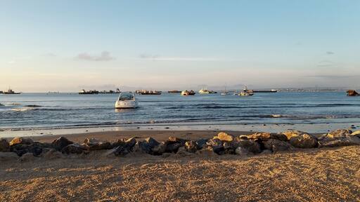 A beach with a rocky shoreline and several boats in the water.