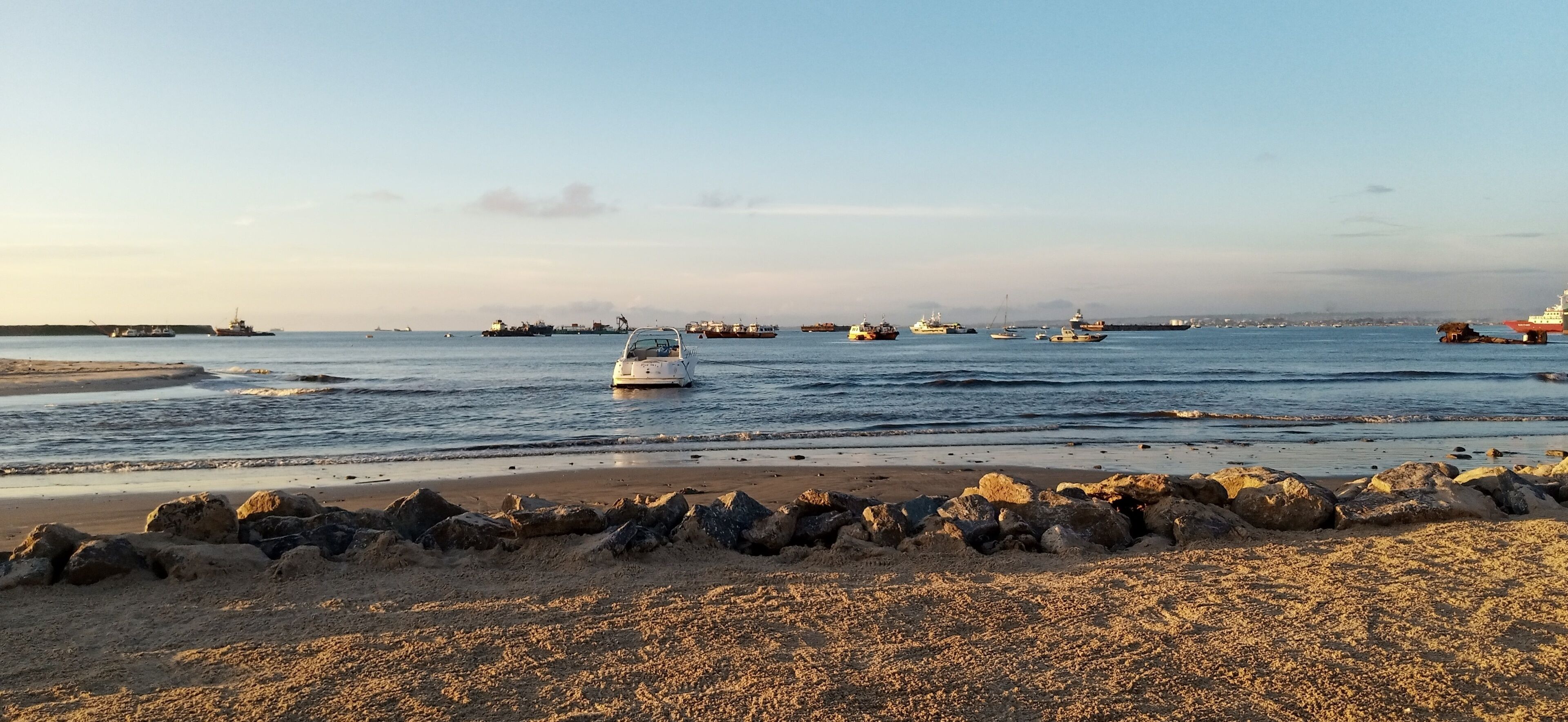 A beach with a rocky shoreline and several boats in the water.