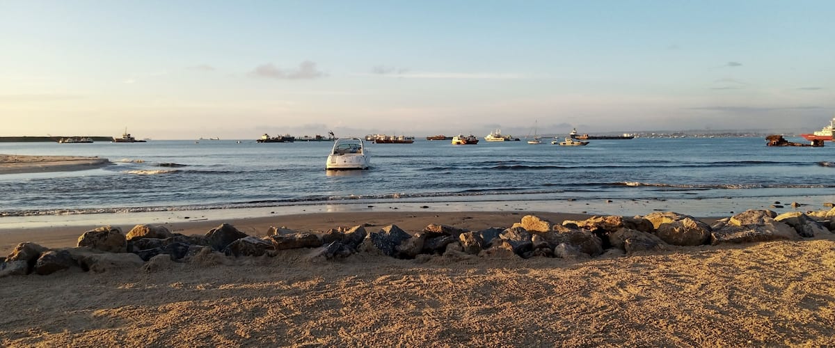 A beach with a rocky shoreline and several boats in the water.