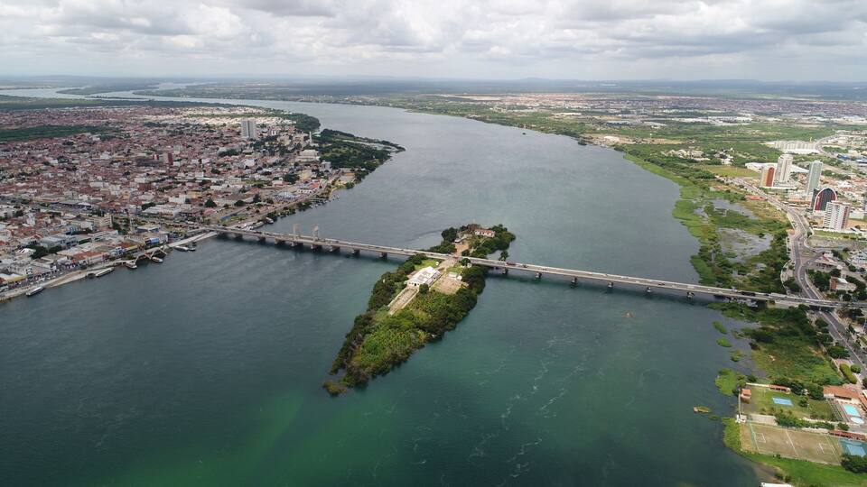A river with a bridge, a cityscape, and a green island.