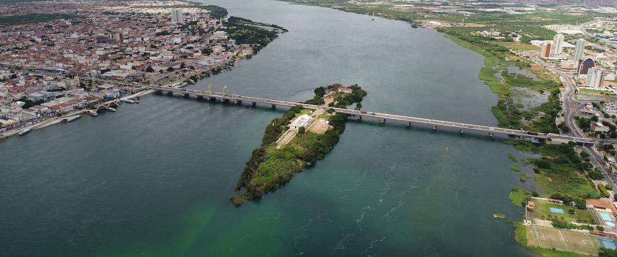A river with a bridge, a cityscape, and a green island.