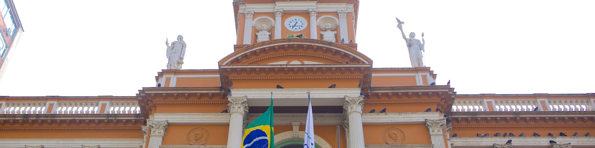 A grand building with a clock tower, statues, and flags.