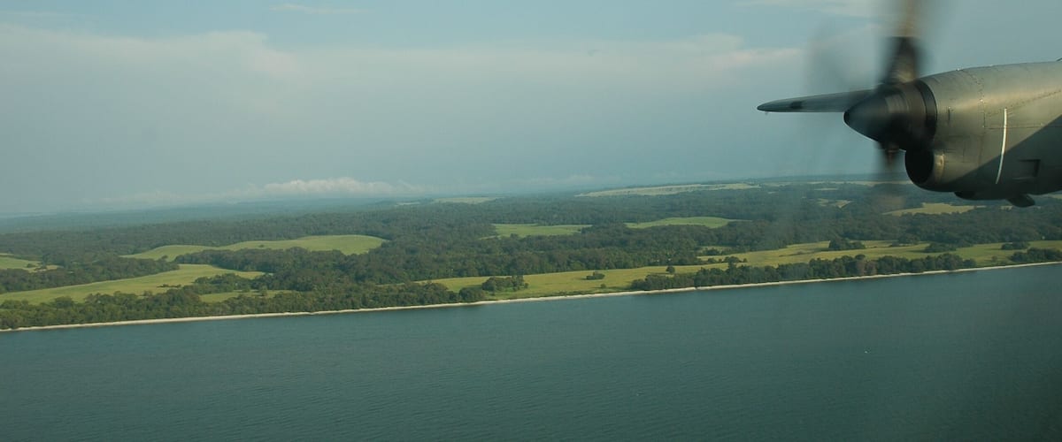 An airplane flying over a coastal landscape with green fields and a body of water.
