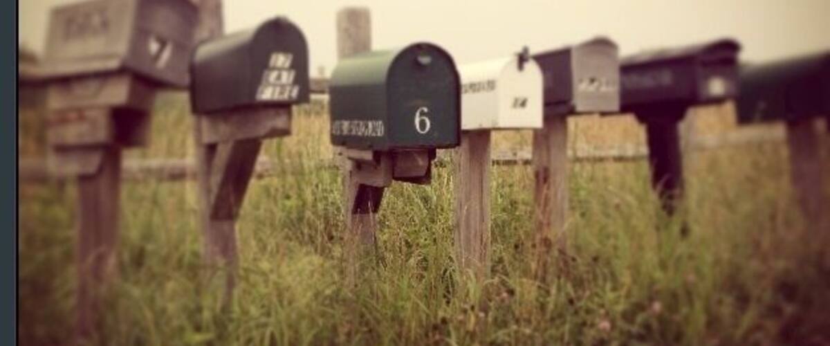 A row of mailboxes in a grassy area with a dirt path.
