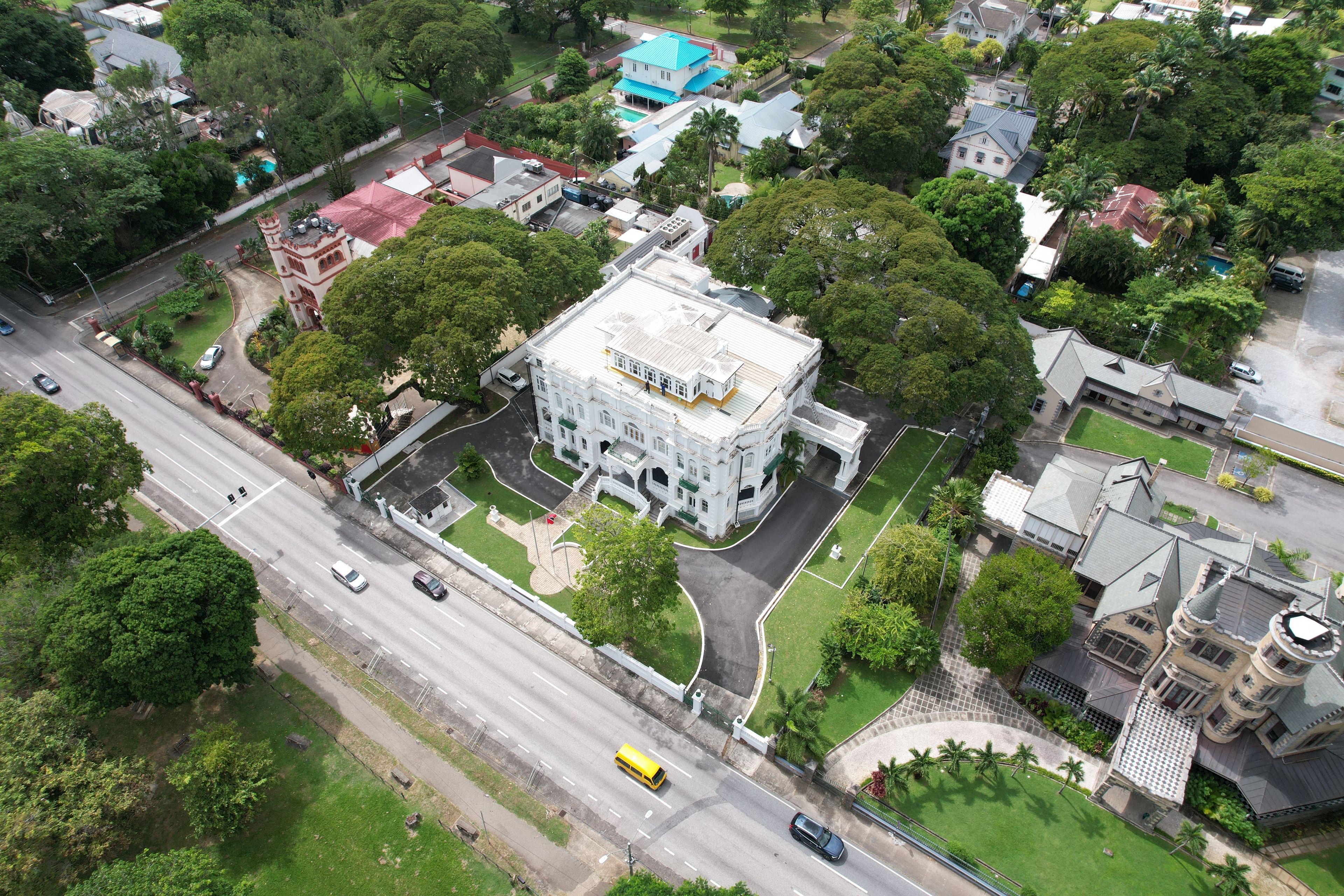 An aerial view of a cityscape with a prominent white building with a green roof, surrounded by lush greenery and other residential buildings.