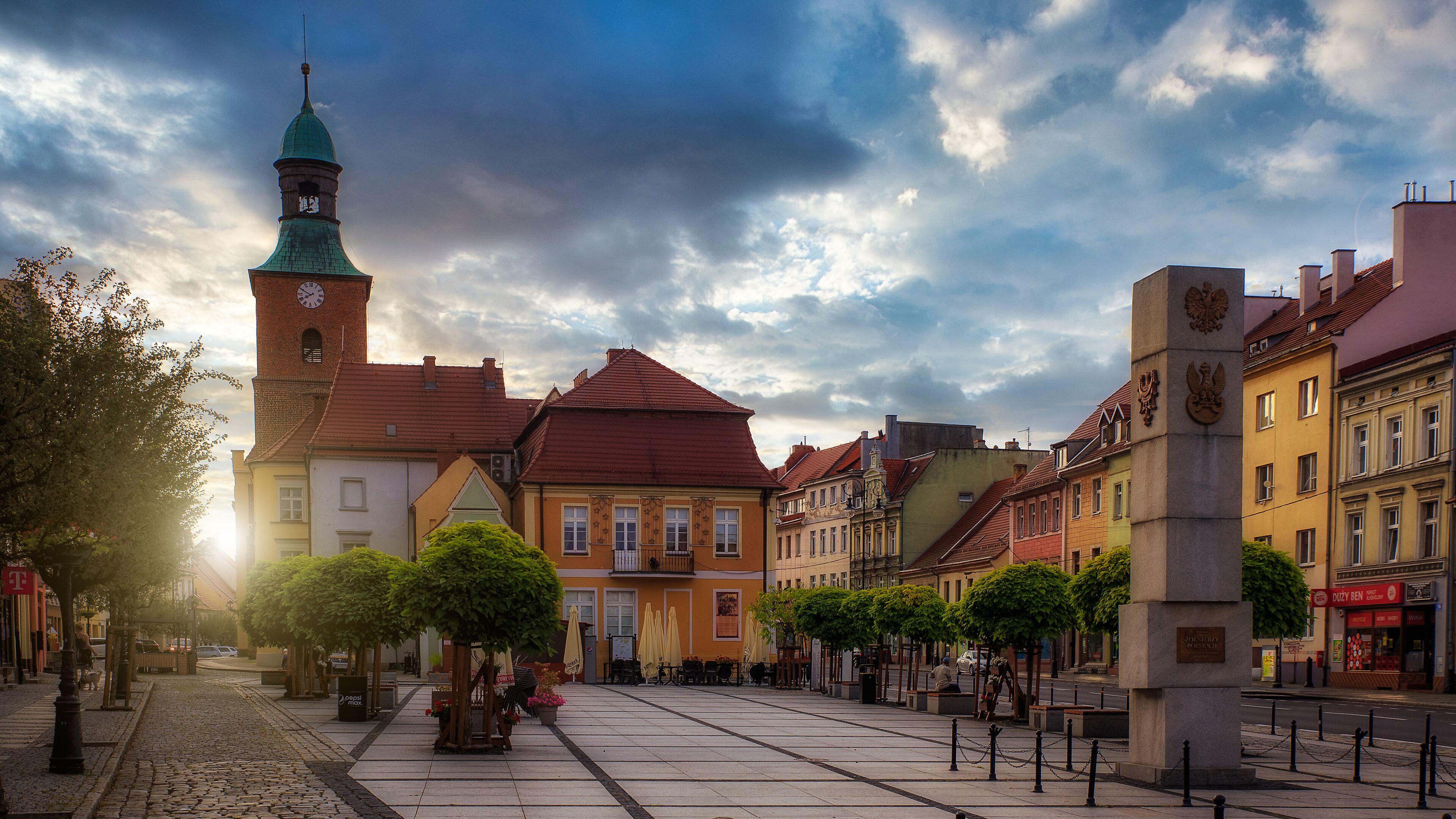 A historic square with a prominent clock tower, traditional buildings, and a statue.