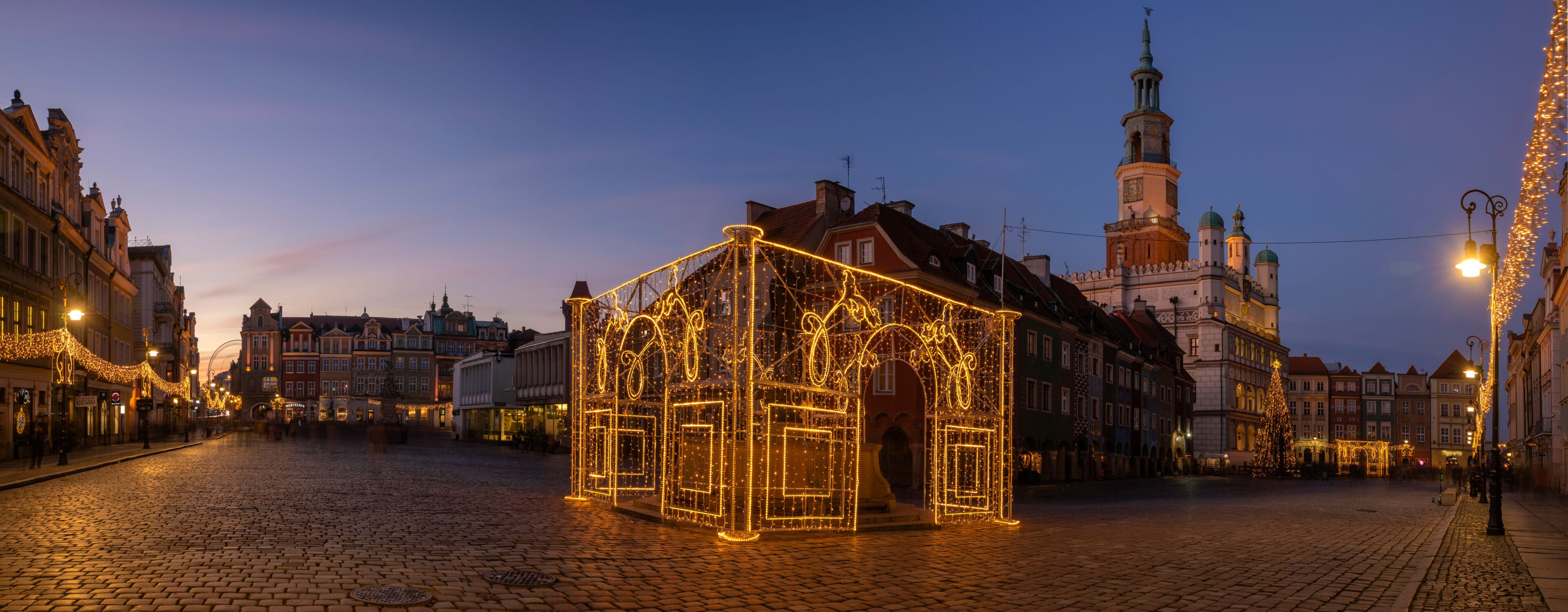 A cobblestone square with a decorated gazebo and historic buildings in the background.