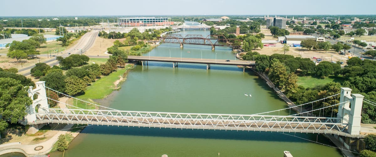 A suspension bridge over a river with a cityscape in the background.