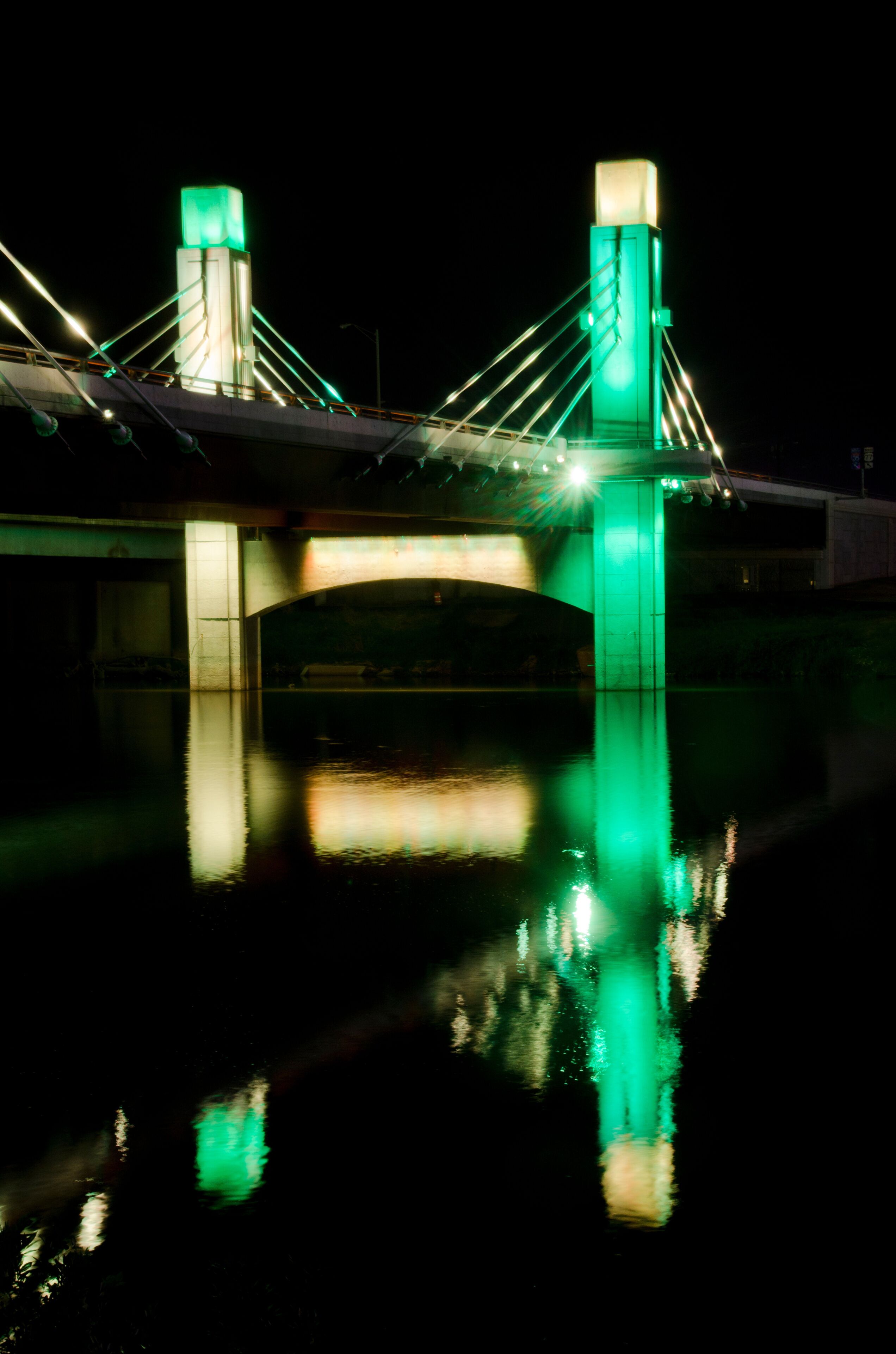 A bridge with green lights and its reflection on water.