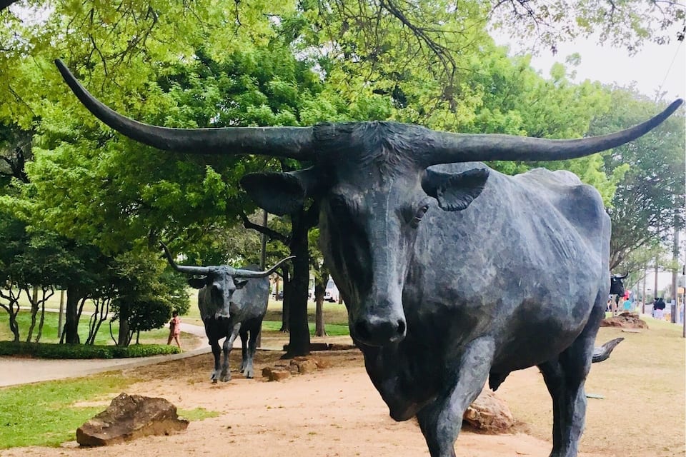 A large black ox statue in a park with trees and a dirt path.