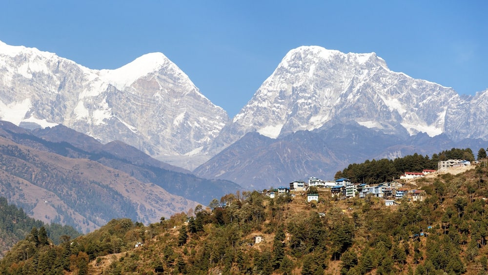 A mountainous landscape with snow-capped peaks and a cluster of buildings on a hillside.