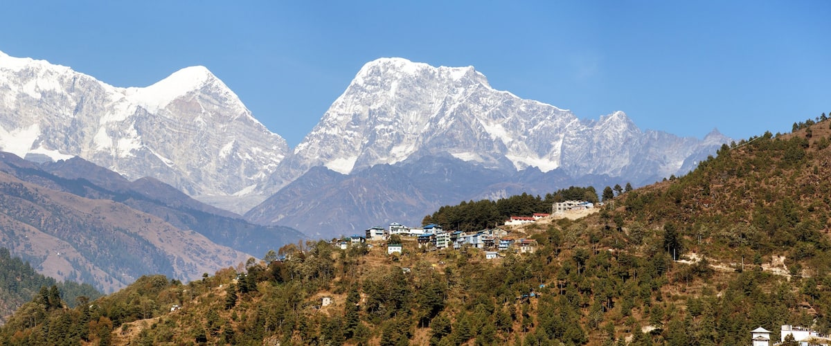 A mountainous landscape with snow-capped peaks and a cluster of buildings on a hillside.