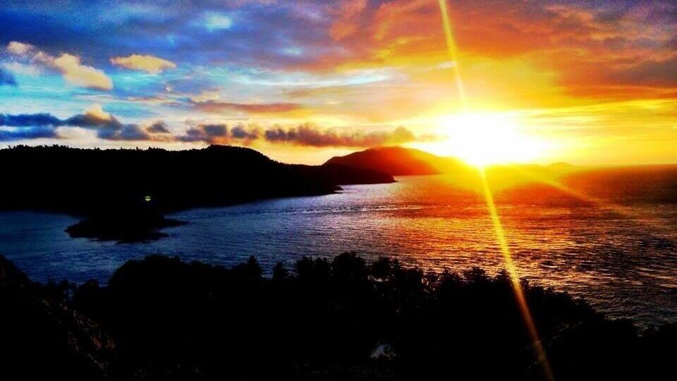 A sunset over a body of water with silhouetted landforms in the foreground.