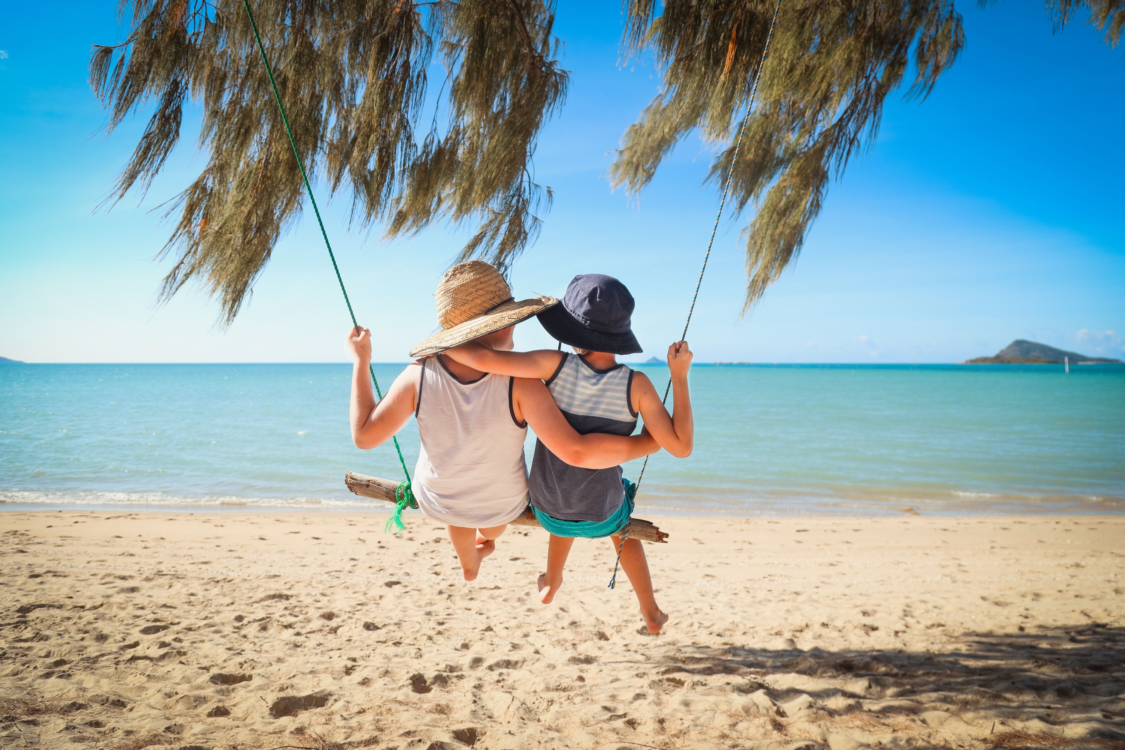Two people on a beach swing, with a clear blue sky and calm sea in the background.