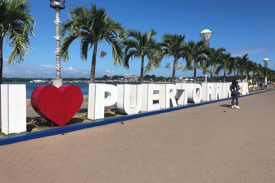 A coastal promenade with palm trees, a large heart-shaped sculpture, and the words "PUERTO RICO" on a white wall.