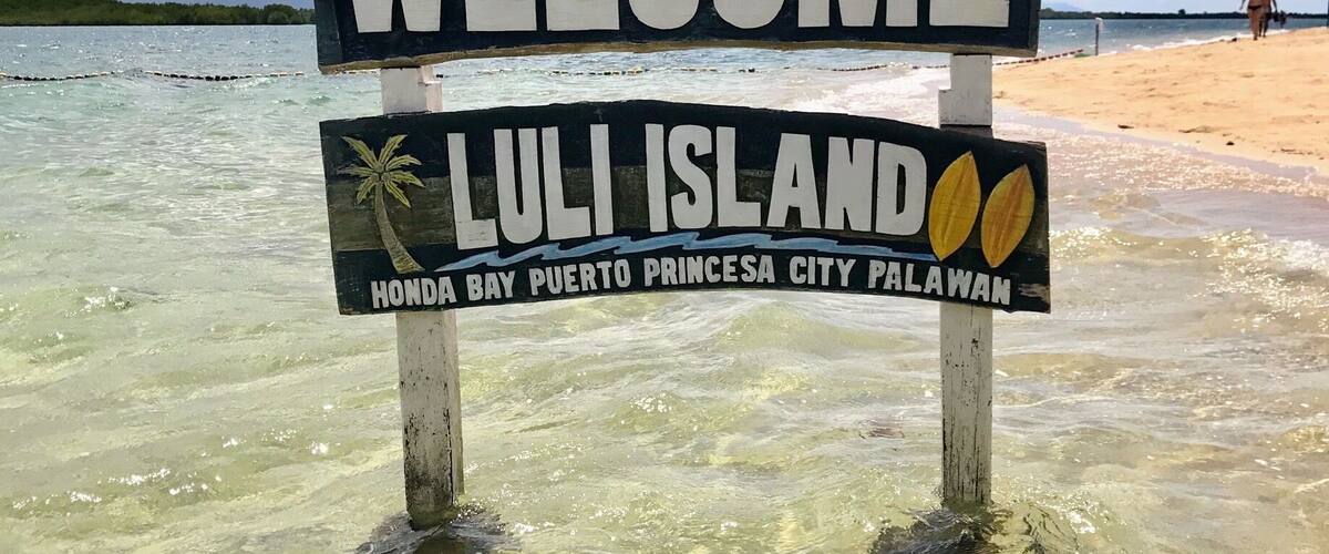 A welcome sign for Luli Island with dolphins and palm trees.