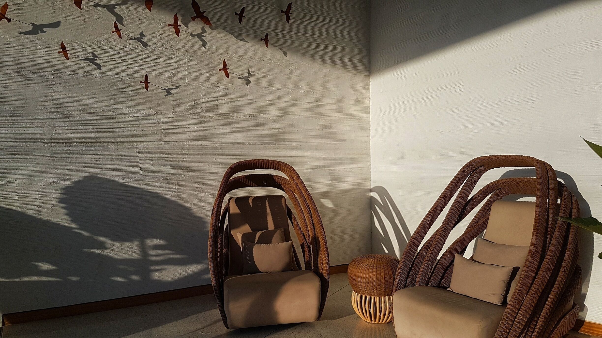 A room with wicker chairs, a wall with bird silhouettes, and a small round table.