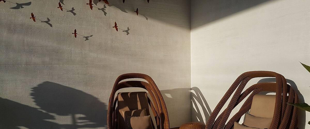 A room with wicker chairs, a wall with bird silhouettes, and a small round table.