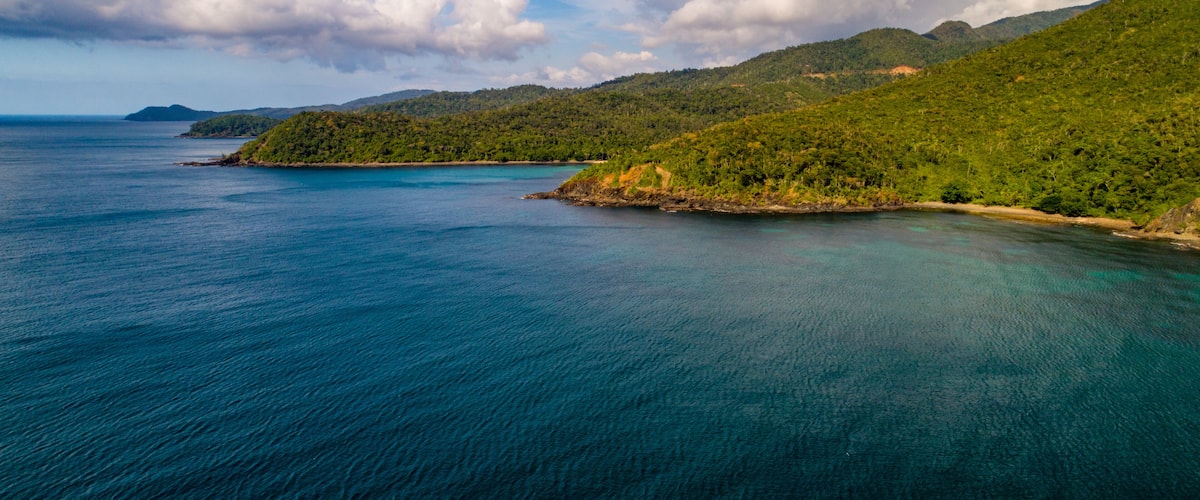 A coastal landscape with a clear blue sea, green hills, and a distant island.