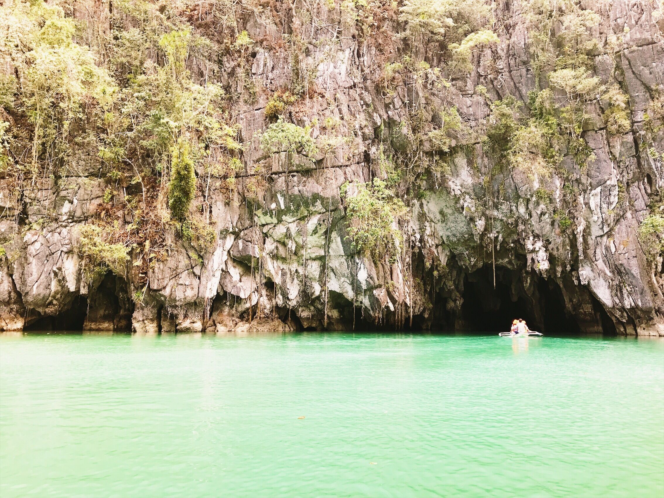 A cave entrance surrounded by rocky cliffs and lush greenery.