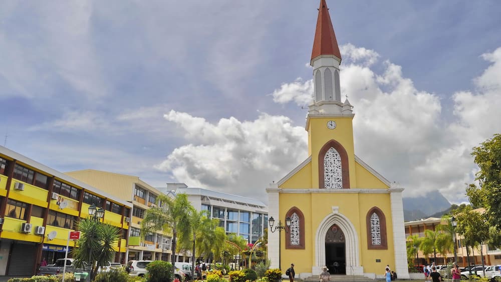 A church with a tall steeple and a clock, surrounded by buildings and people.