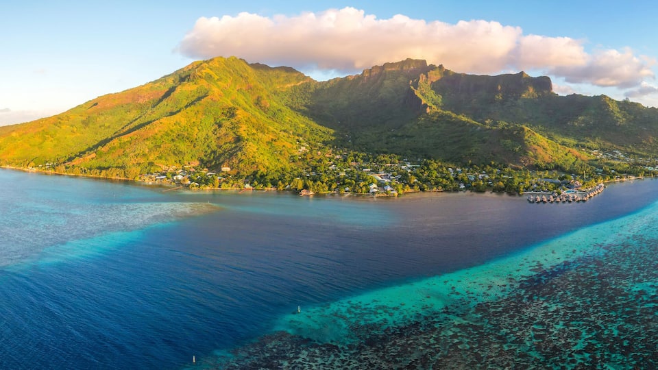 A tropical island with a prominent mountain, clear turquoise waters, and a small settlement.