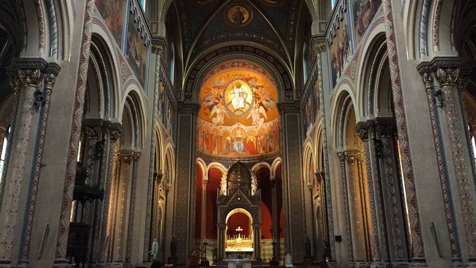An ornate church interior with high vaulted ceilings, detailed frescoes, and a central altar.