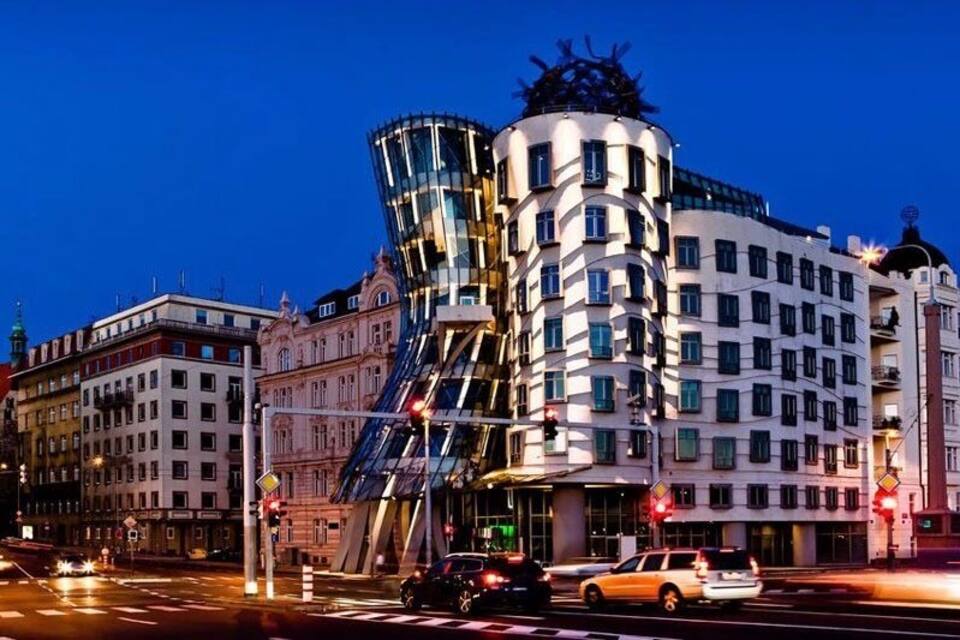 A modern building with a unique curved facade and a traditional building with a dome in the background.