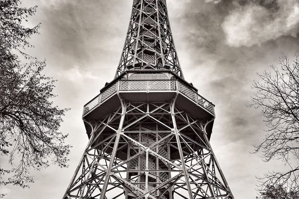 De Eiffeltoren met een ingewikkeld metalen skelet, omringd door bomen en een bewolkte lucht.