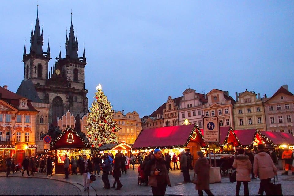 Een levendige kerstmarkt met een grote versierde kerstboom en traditionele gebouwen op de achtergrond.