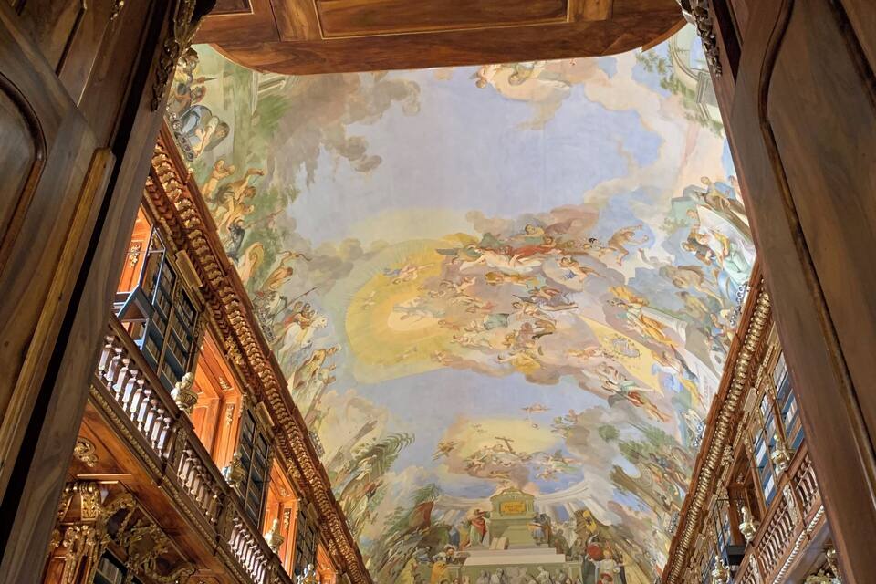 Een weelderig ingerichte bibliotheek met een gedetailleerde plafondfresco en klassieke architectuur.