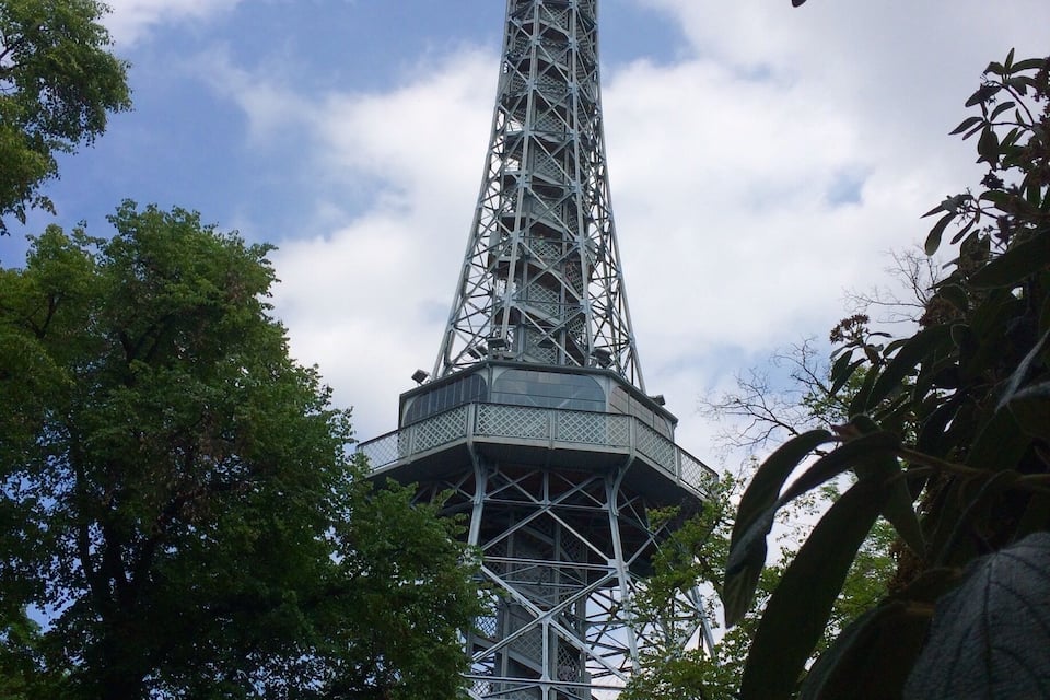 A tall, metal tower with a complex lattice structure, surrounded by lush green trees.