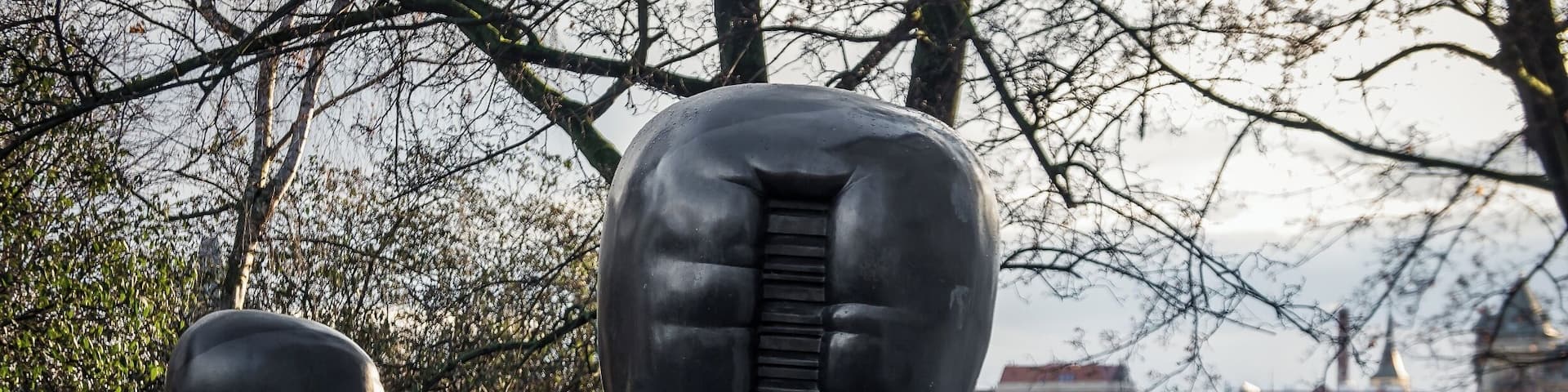 A sculpture of a muscular figure in a crouched position, surrounded by trees and buildings in the background.