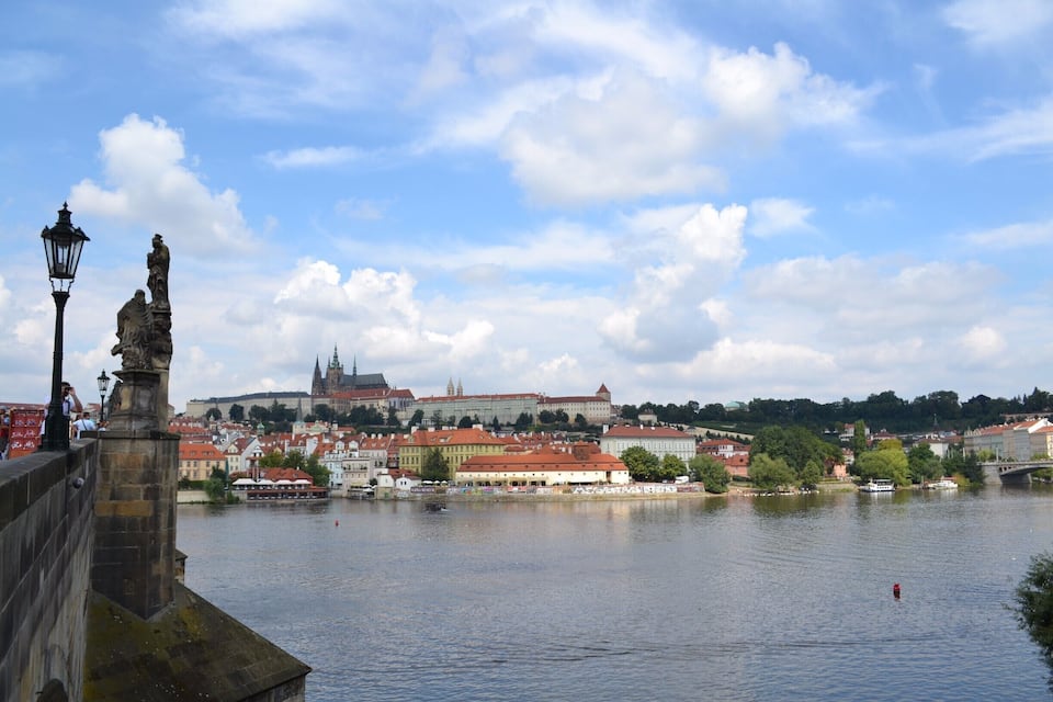 A river with a bridge, a statue, and a historic building in the background.