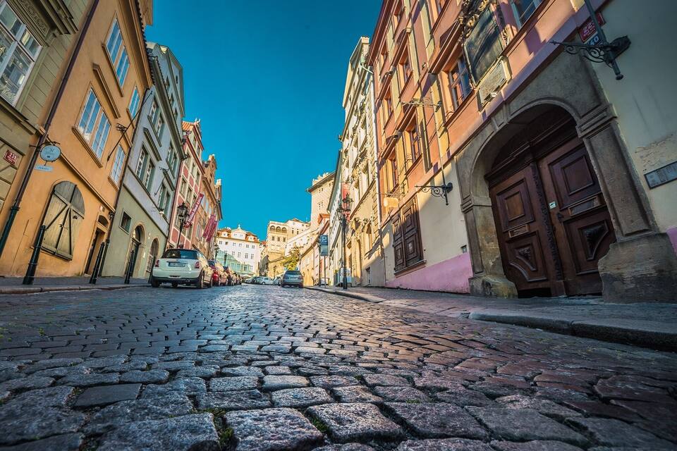 Una calle empedrada bordeada de edificios históricos, un coche estacionado al lado, y un cielo azul despejado.