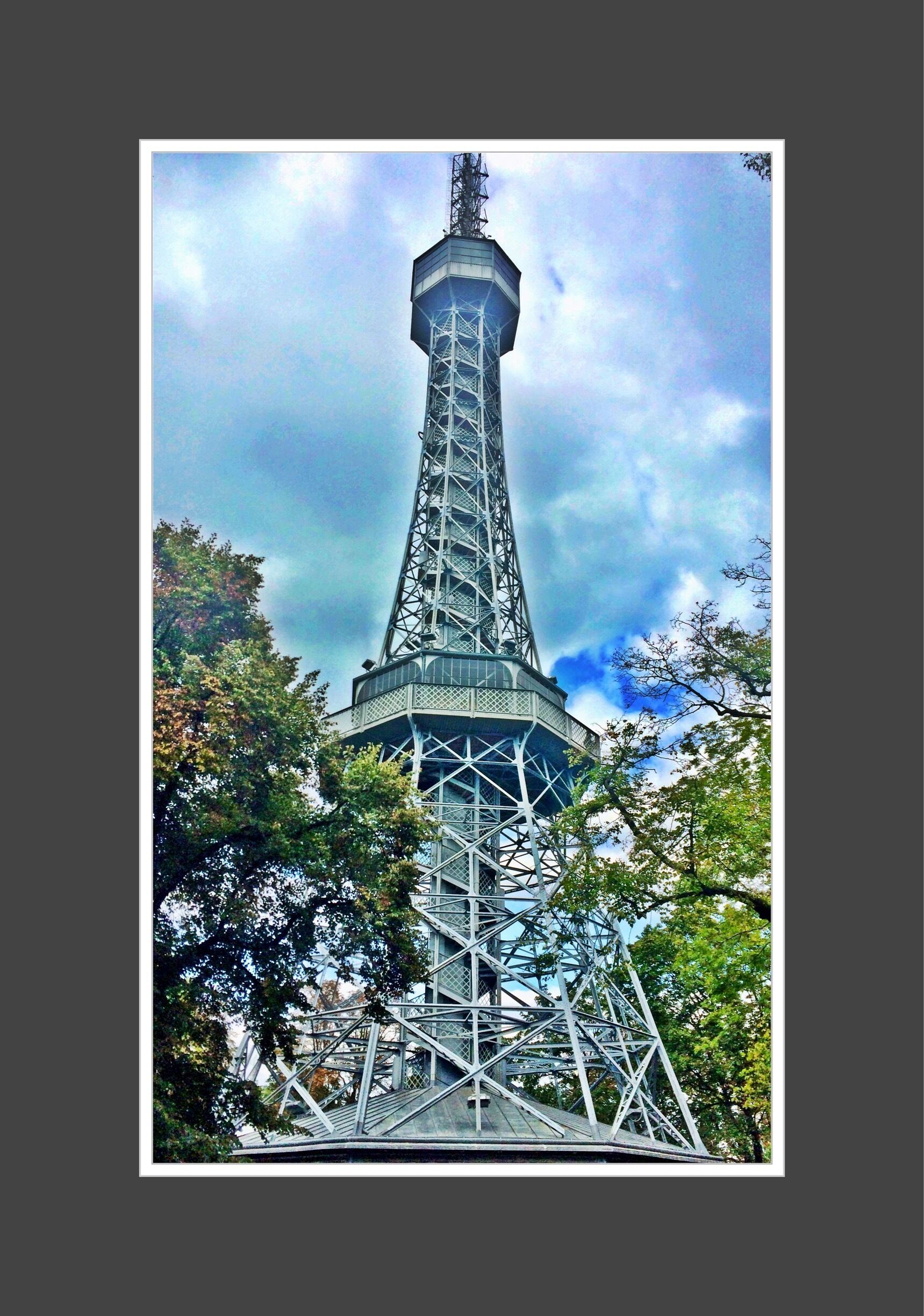 A Torre Eiffel sob um céu nublado e árvores em primeiro plano.