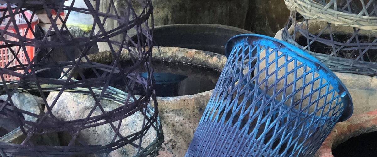 A large, weathered clay pot with a dark liquid inside, surrounded by other pottery and baskets.