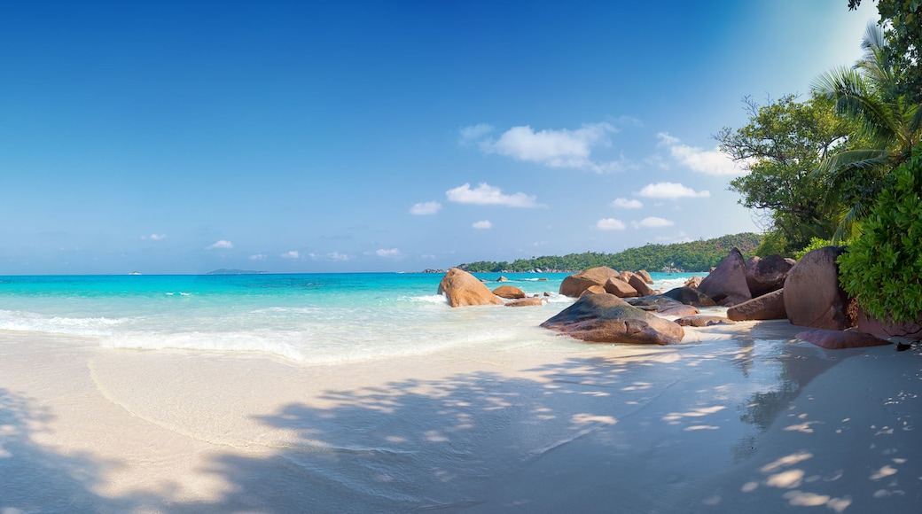 A tropical beach with clear turquoise waters, white sand, and large rocks.