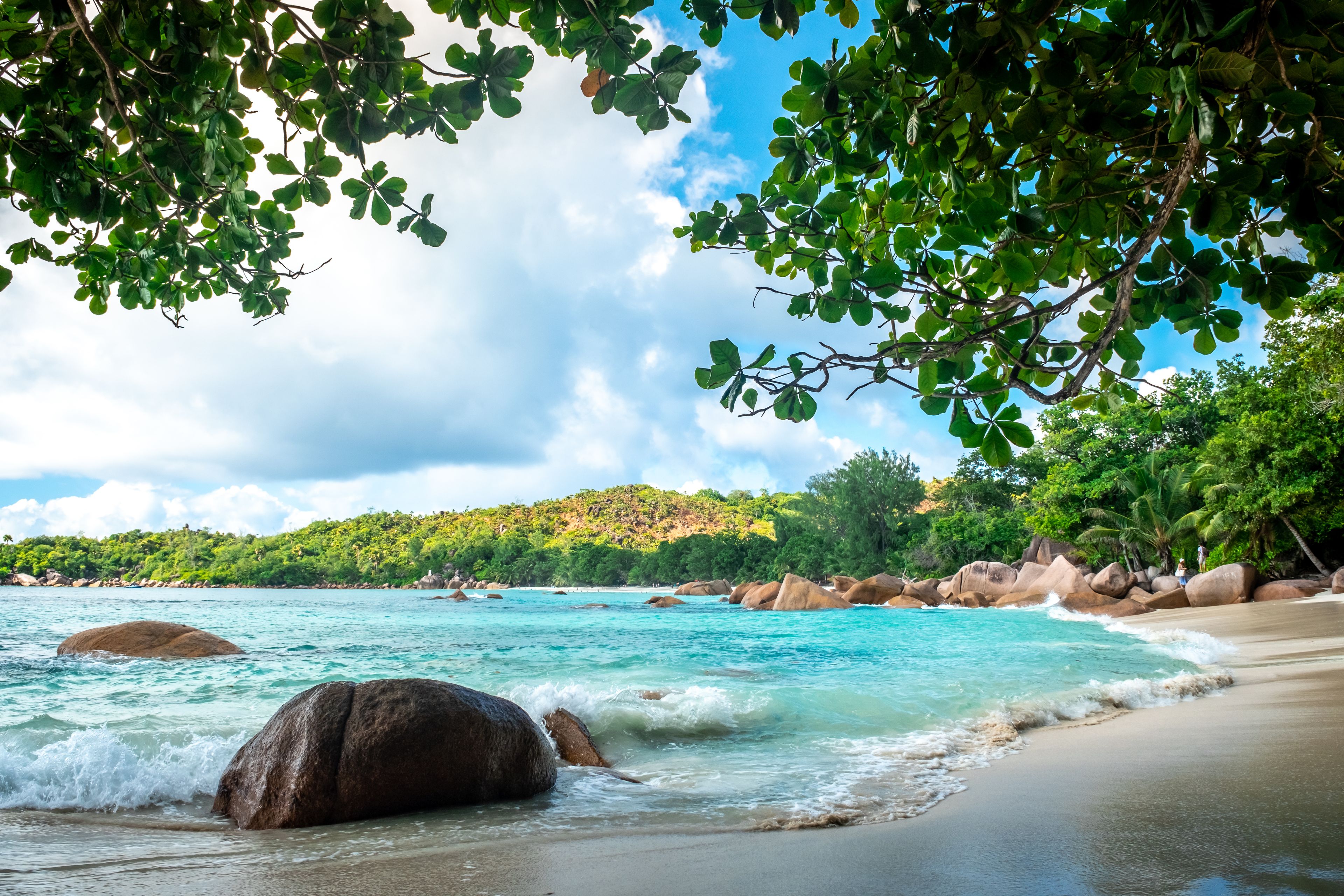 Una playa con aguas turquesas cristalinas, rocas grandes y vegetación verde exuberante.