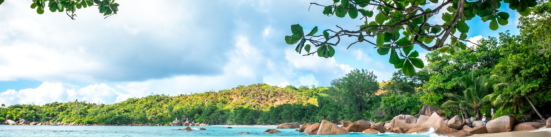 Una playa con aguas turquesas cristalinas, rocas grandes y vegetación verde exuberante.