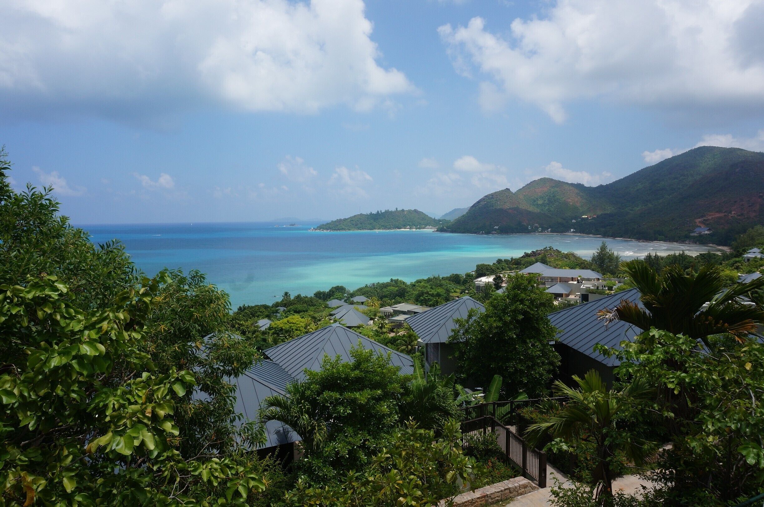 A coastal landscape with turquoise waters, green hills, and residential buildings.