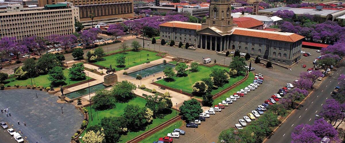 A cityscape with a large building, a central plaza with a statue, and a parking lot.