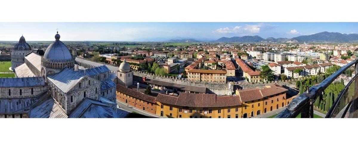 The Pisa Cathedral and the Leaning Tower of Pisa surrounded by historic buildings and a distant view of the countryside.