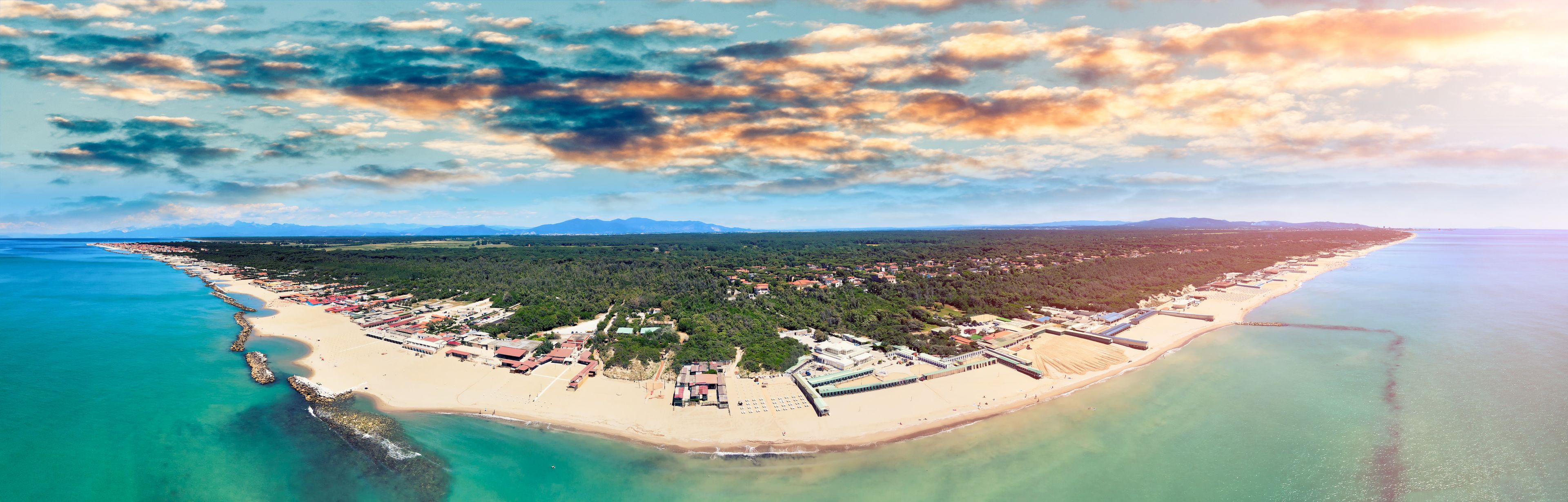 Un pueblo costero con playa, muelle y montañas al fondo.