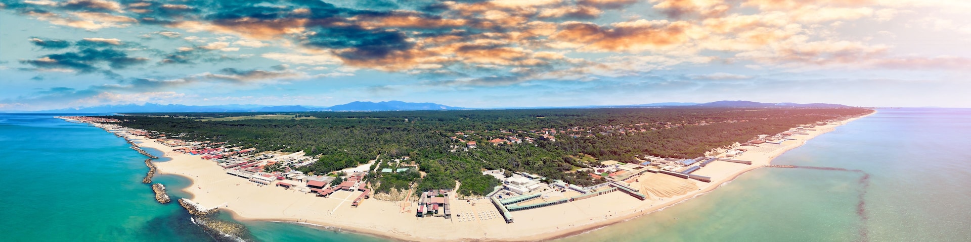 Un pueblo costero con playa, muelle y montañas al fondo.