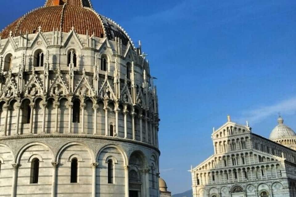 The Pisa Cathedral with its famous leaning dome, the adjacent Baptistery, and a grassy area in front.