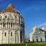 Der Dom von Pisa mit seiner berühmten schiefen Kuppel, das angrenzende Baptisterium und eine grüne Fläche davor.