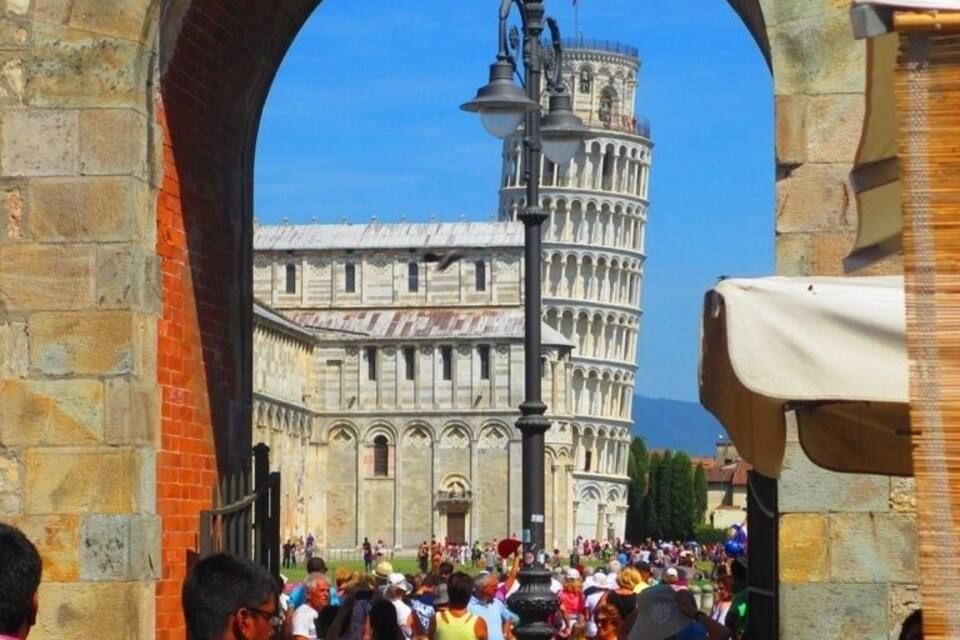 A crowd of tourists at the Leaning Tower of Pisa, viewed through an archway.